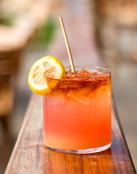 a glass of orange drink with a lemon slice and ice