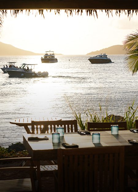 a table and chairs on a beach with boats in the water