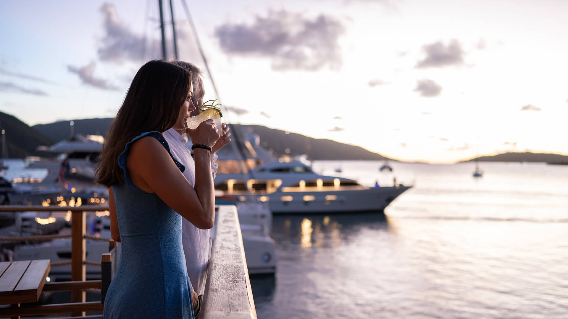 two women drinking from a glass on a railing overlooking a body of water