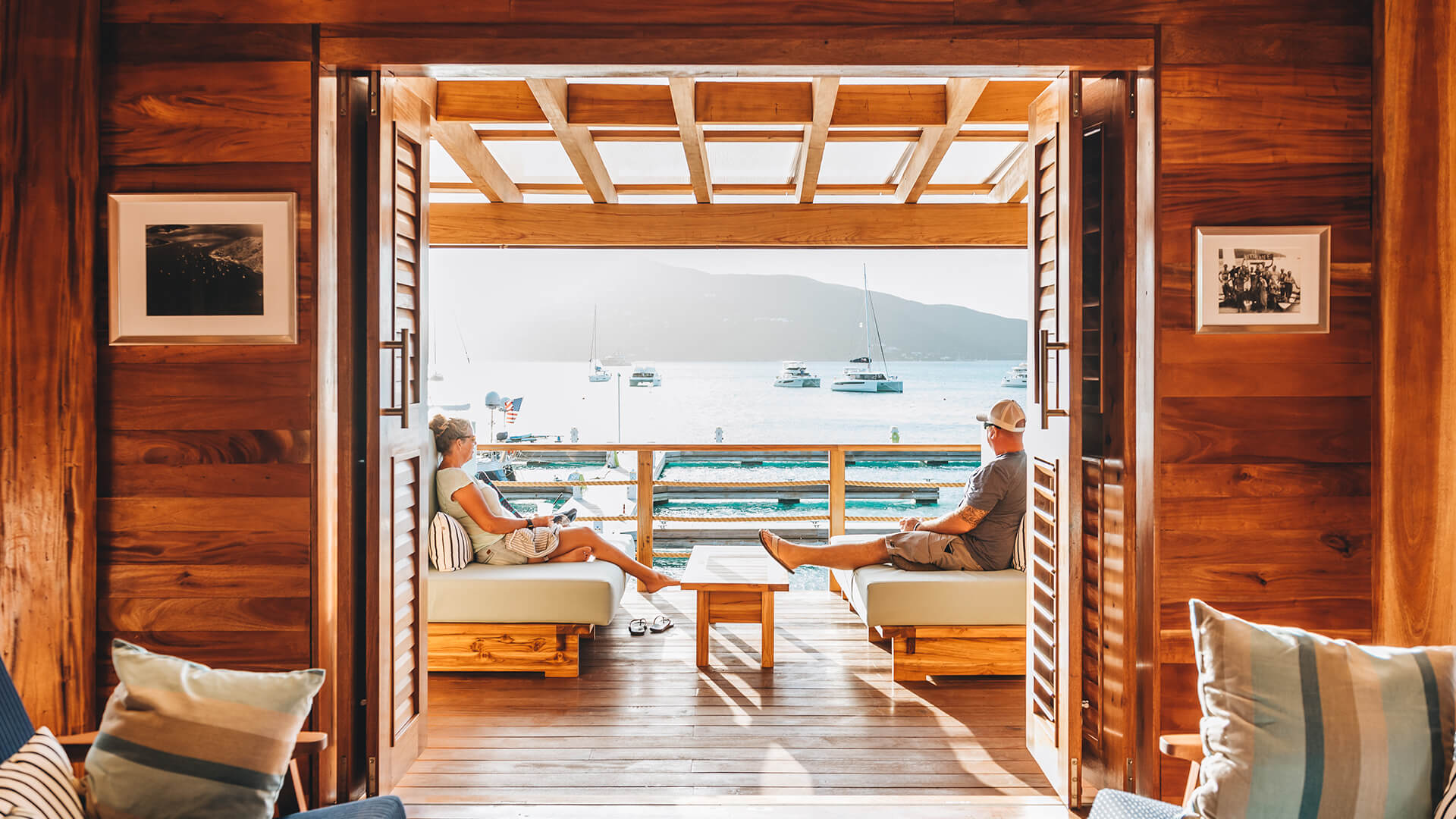 a man and woman sitting on couches on a deck overlooking water