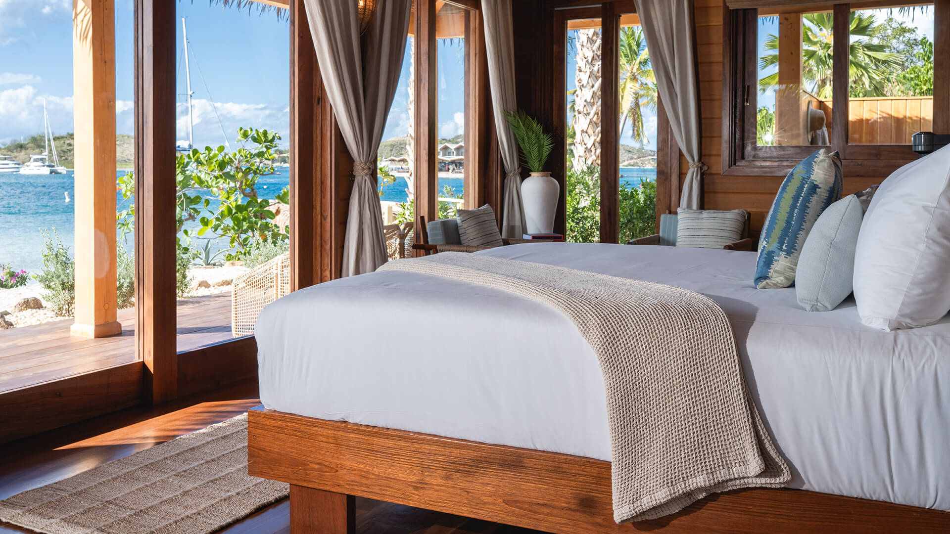 a bed with a blanket and chairs in a room with a view of the ocean