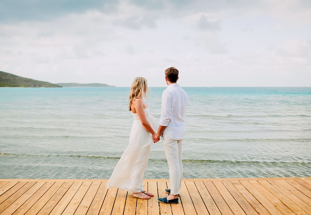 a man and woman holding hands on a dock by the water