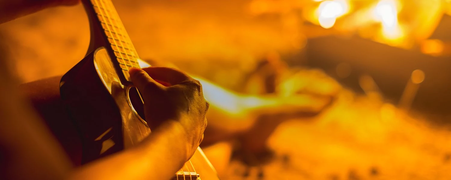 close up of a person playing the guitar at a beach bonfire