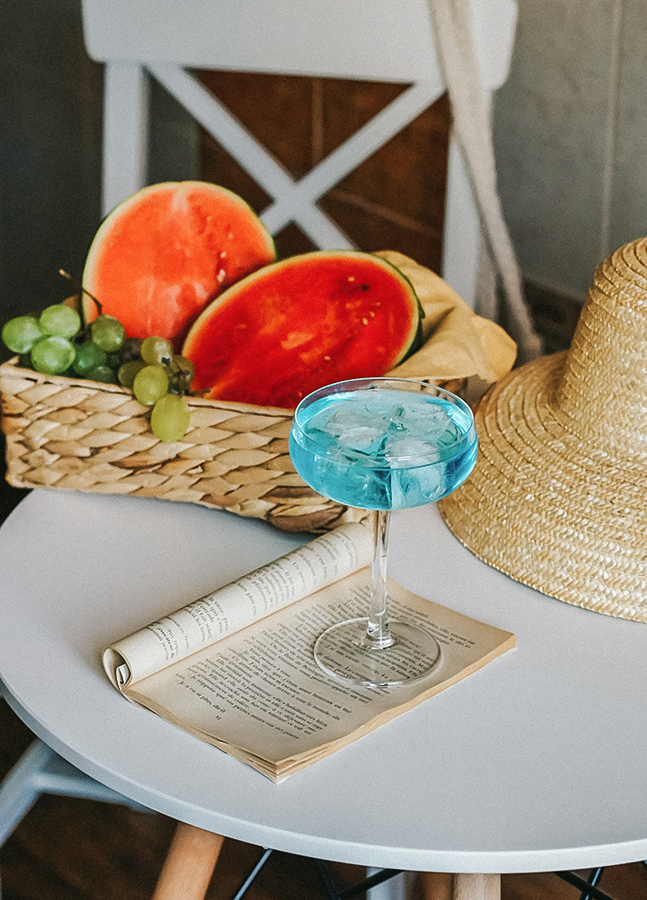 a glass of blue liquid on a table next to a basket of fruit