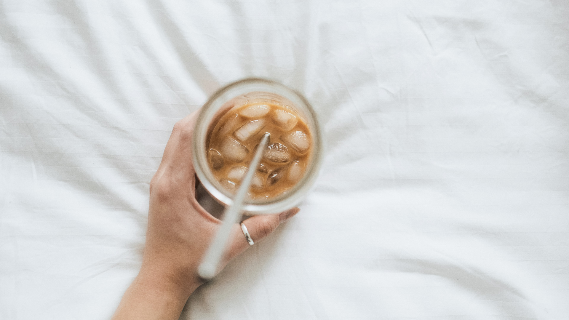 a hand holding a glass with ice and a straw