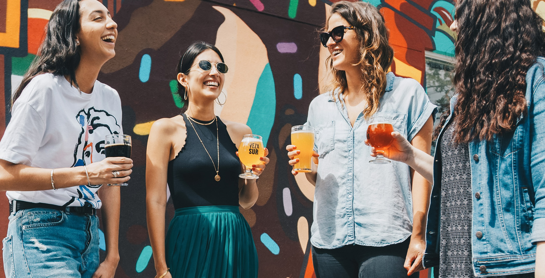 two women holding drinks in front of a colorful wall