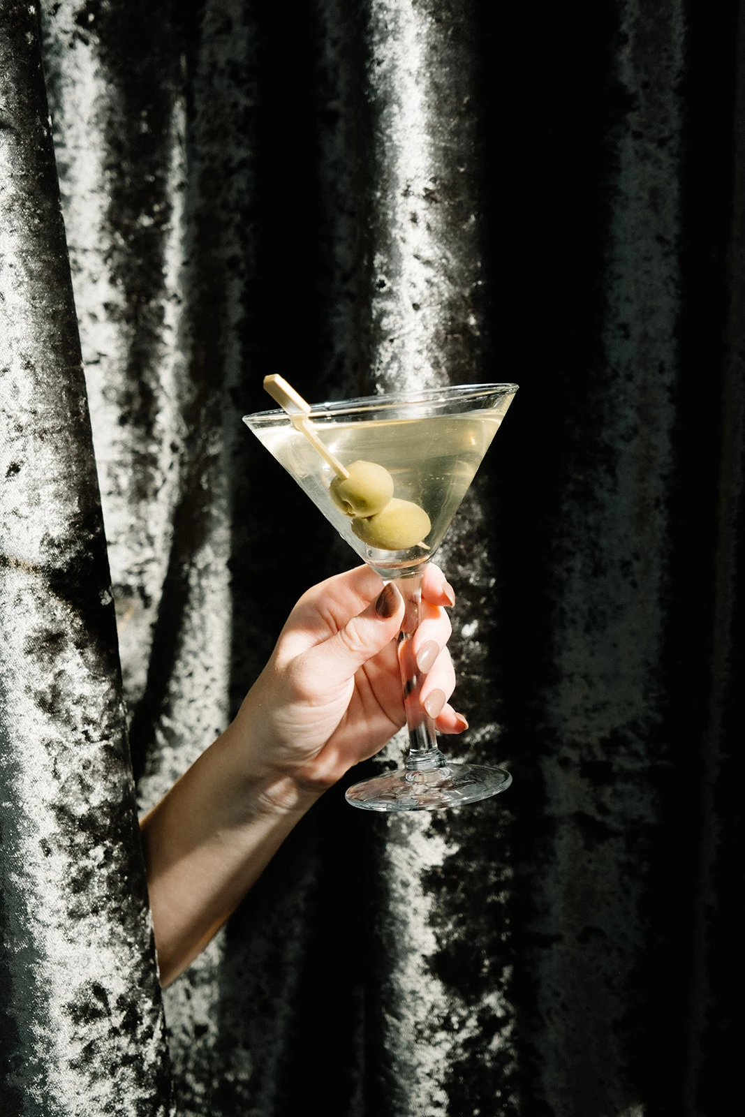 a hand holding a martini glass with olives