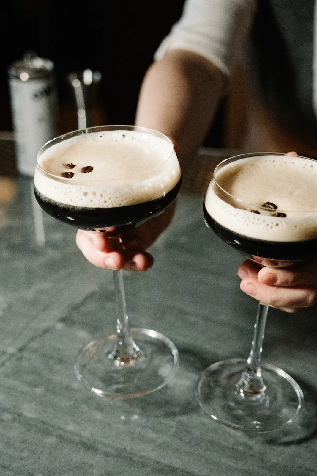 two hands holding glasses with brown liquid
