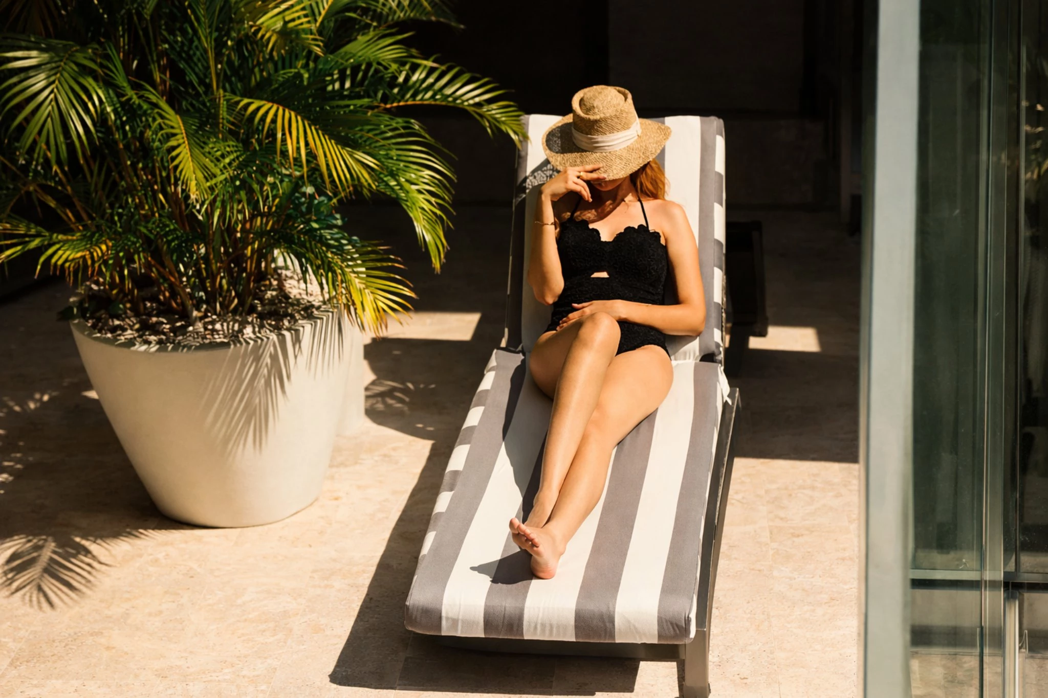 a woman in a swimsuit and hat sitting on a lounge chair