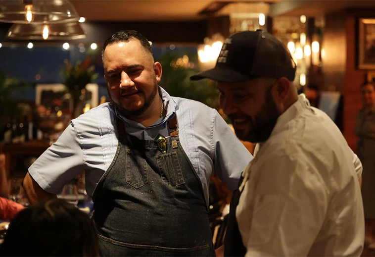 a man in an apron and a baseball cap talking to another man