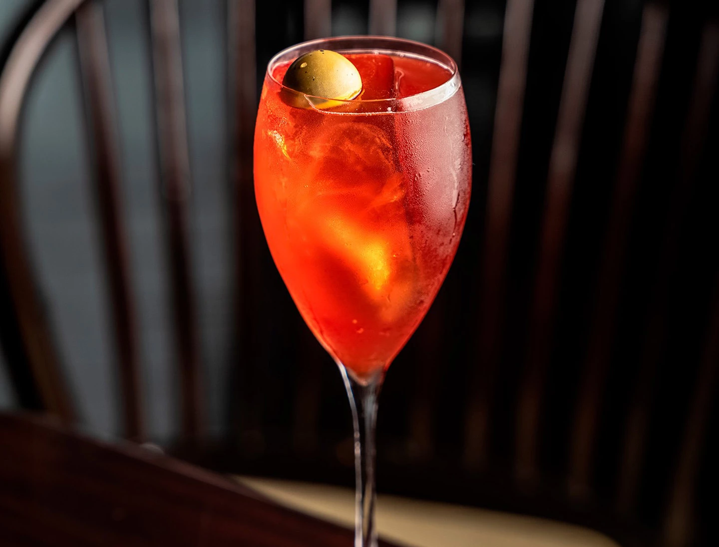 a glass of red liquid with a green olive on top