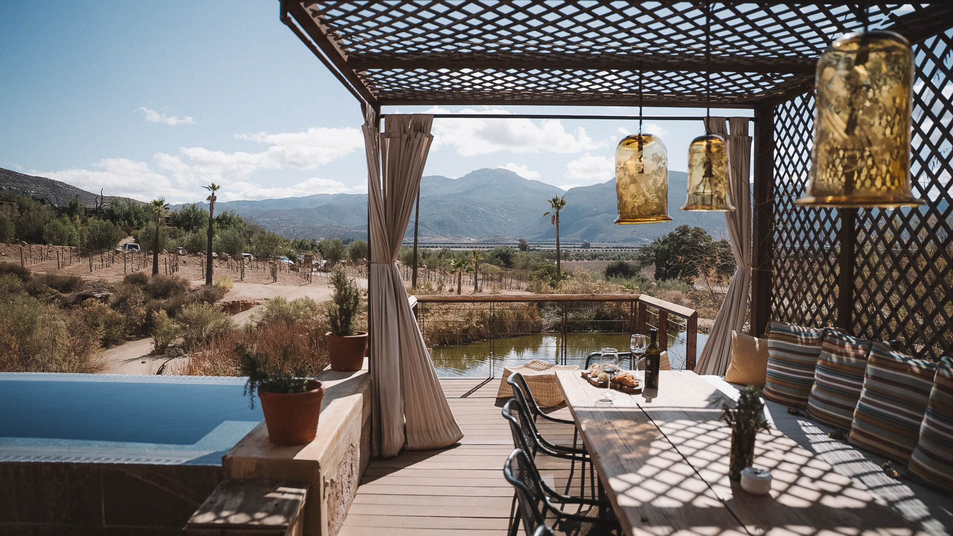 a table and chairs on a deck with a pool and mountains in the background