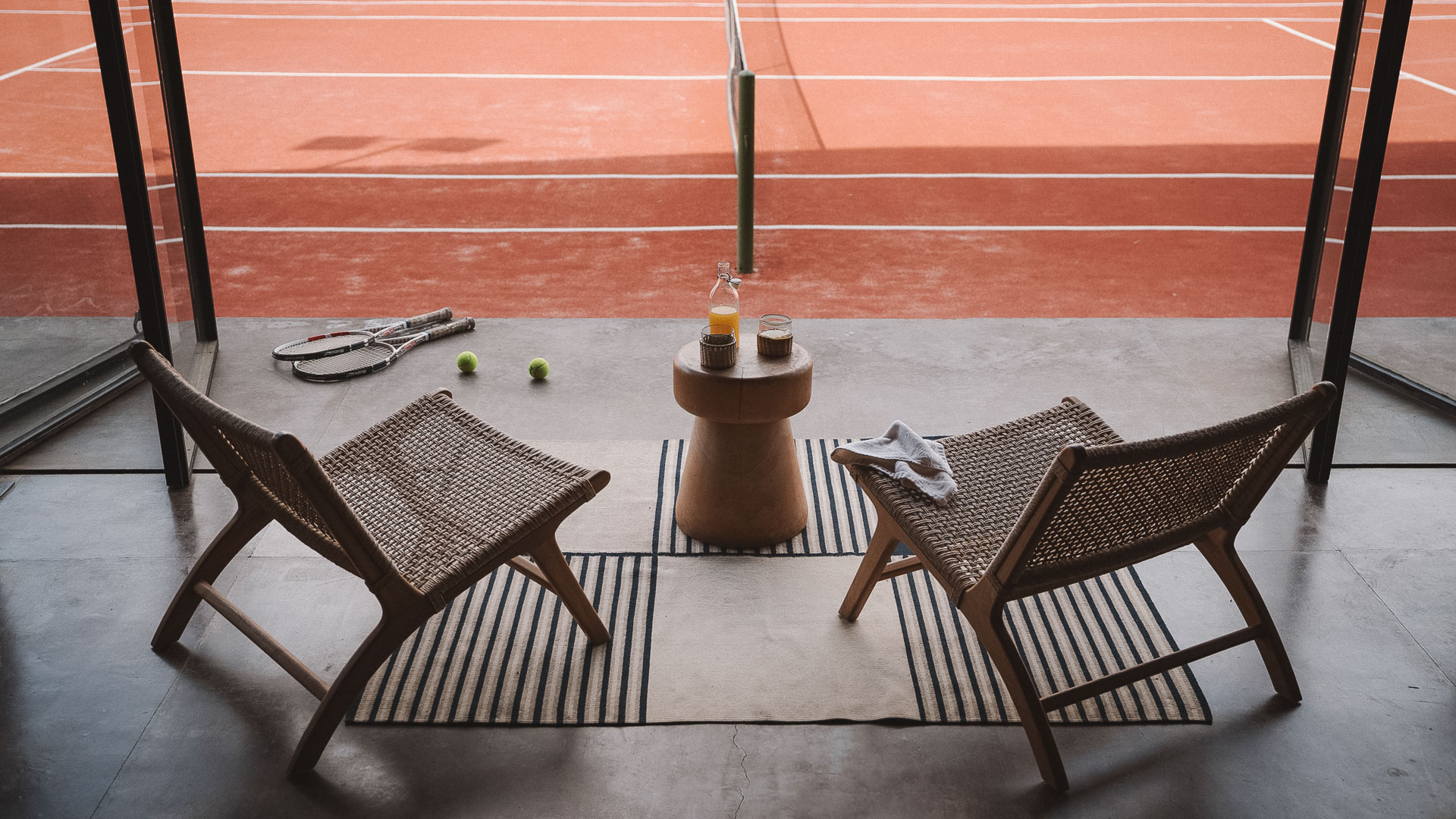 a tennis racket and two chairs on a rug on a tennis court