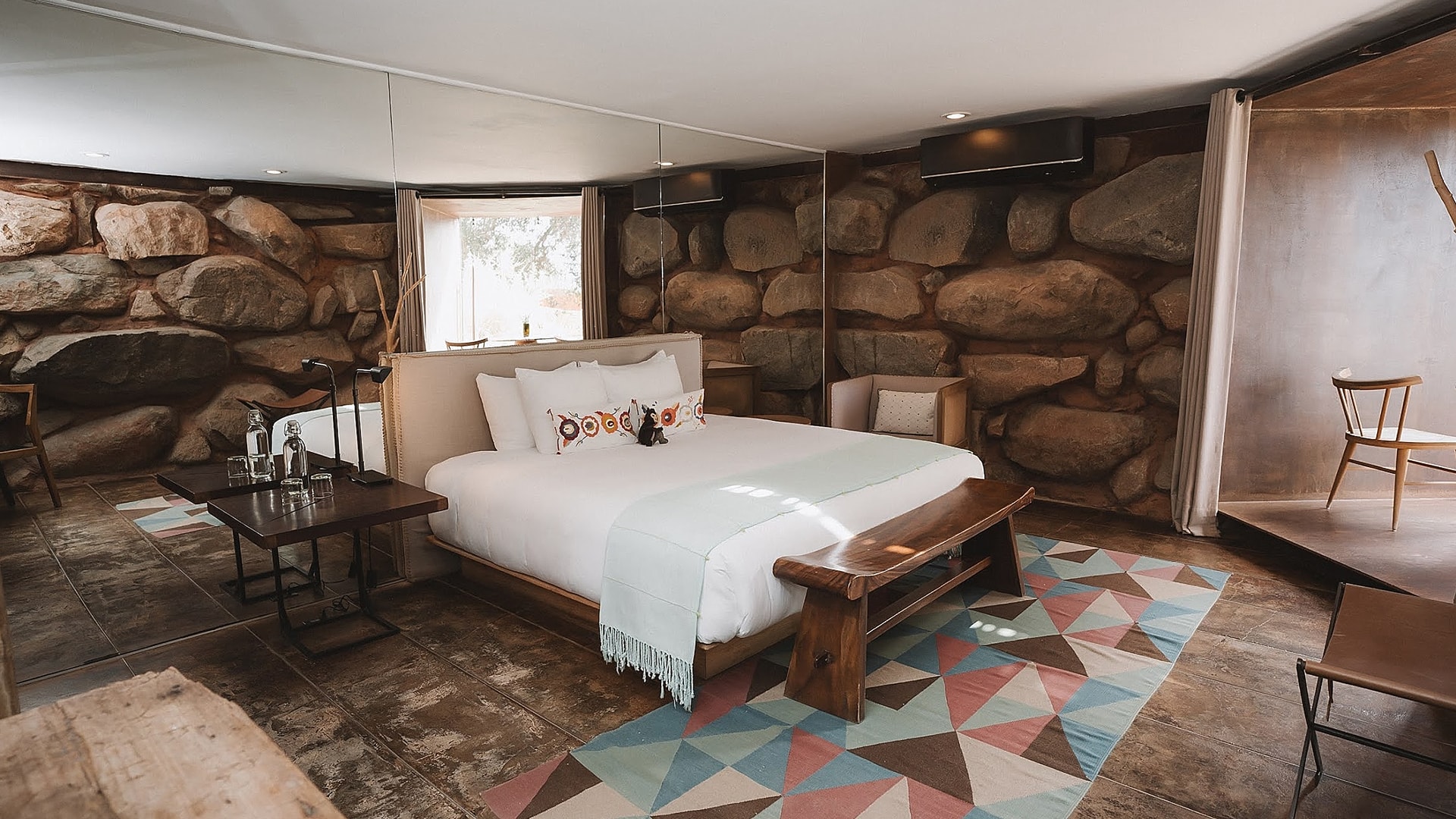 a bed with a bench and a rug in a room with rocks