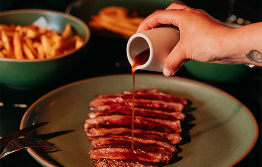 a person pouring sauce on meat