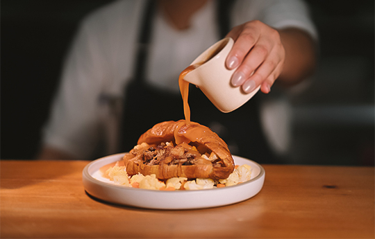 a person pouring sauce over a sandwich