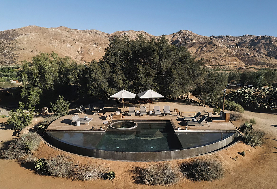 a pool with a wood deck and umbrellas in the middle of a desert