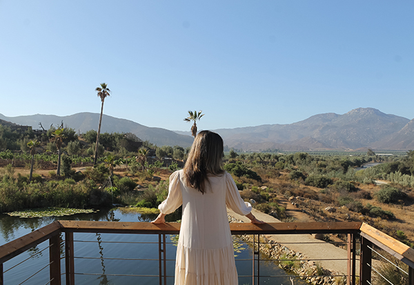 a woman standing on a railing overlooking a river and mountains