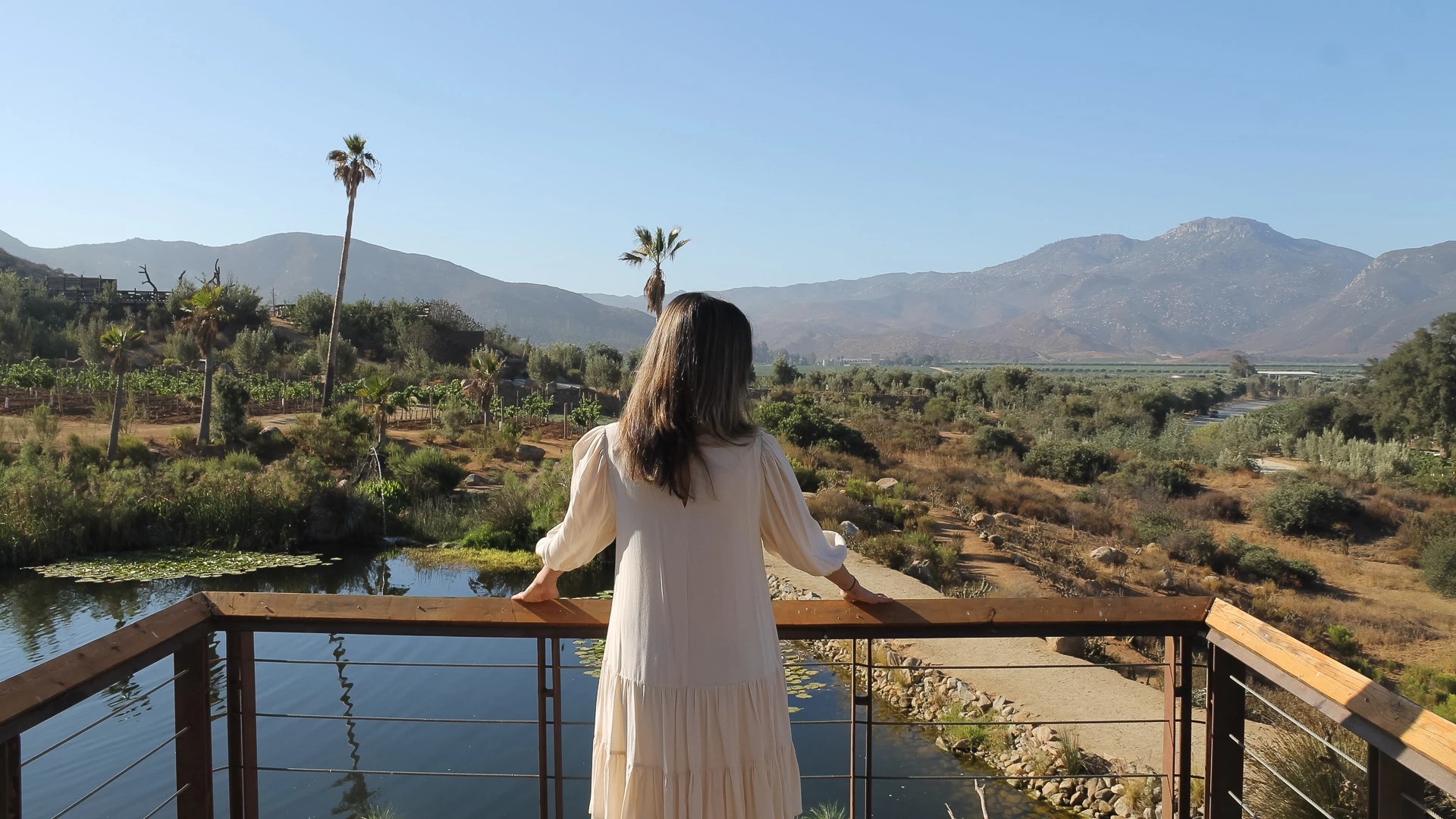 a woman standing on a railing overlooking a river and mountains