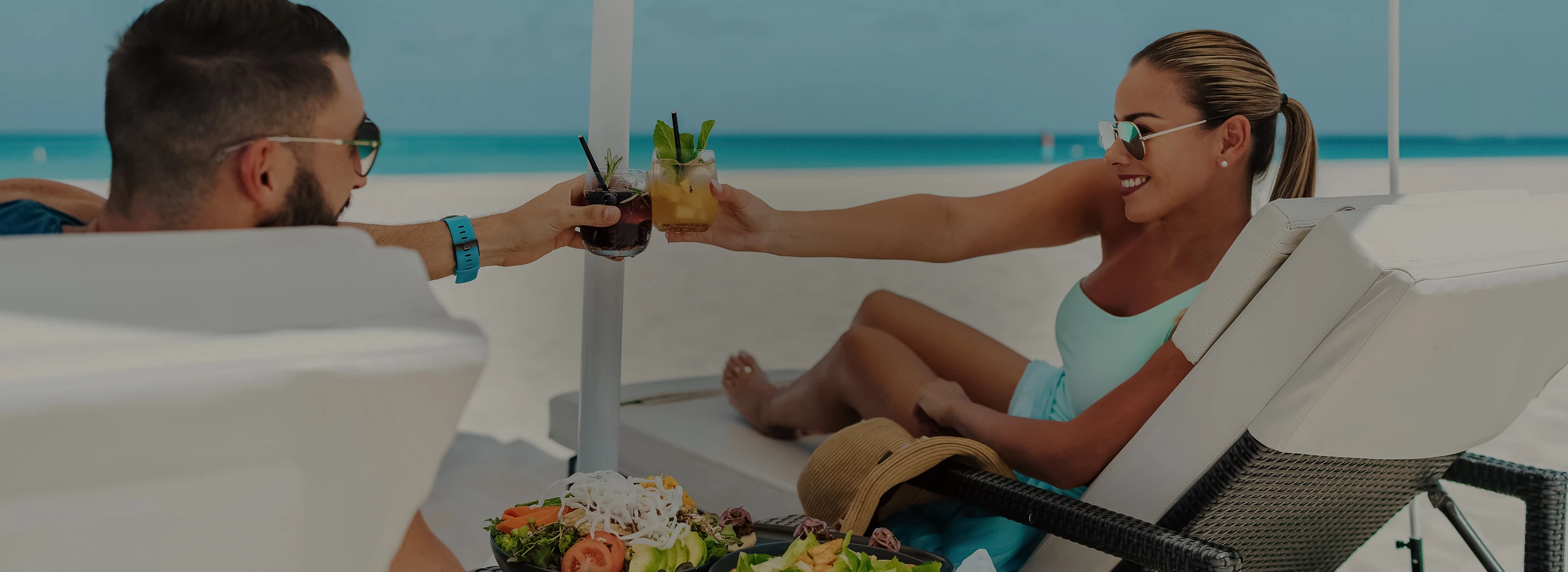 a couple of people sitting on a beach with drinks