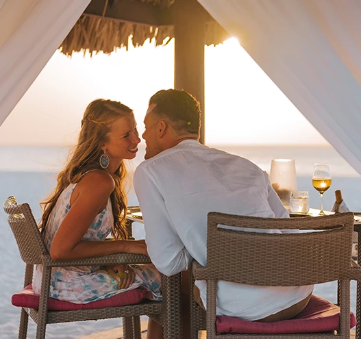 a man and woman sitting at a table with drinks and a straw umbrella
