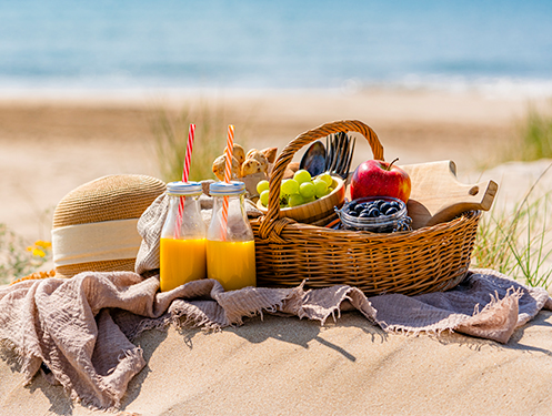 a picnic basket with fruit and juice on a blanket on a beach