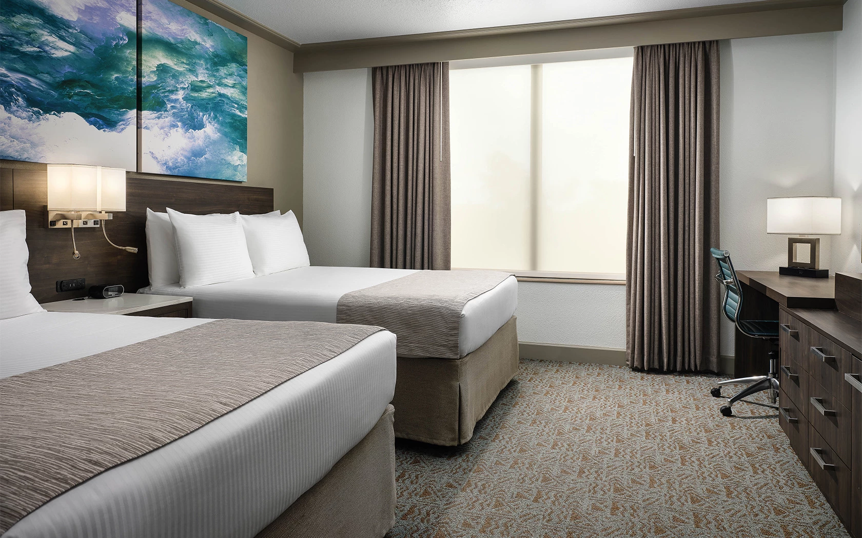 A hotel room with two queen beds, a desk, and a window