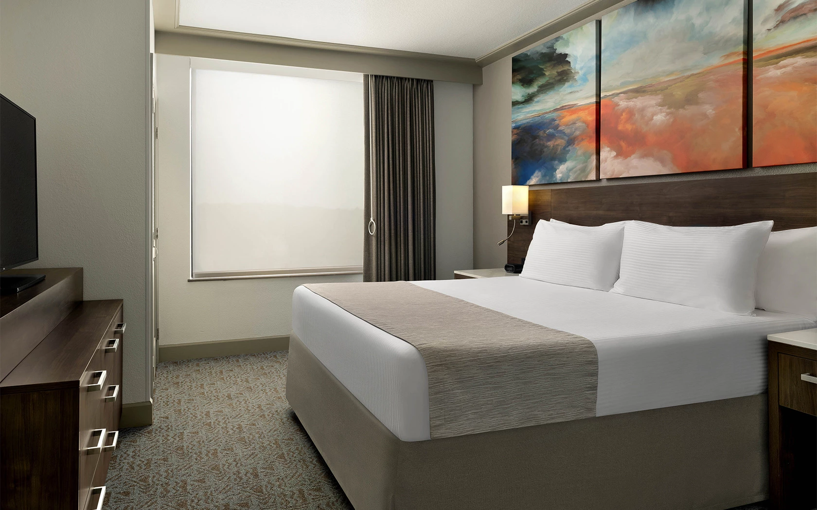 A hotel room with a large bed, TV, and window
