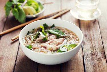 A large bowl of ramen served with a cup of hot tea and chop sticks.