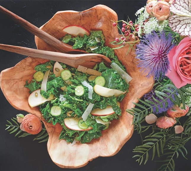 a salad in a wooden bowl next to flowers