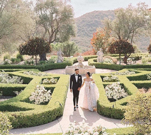 a man and woman in formal wear walking in a garden
