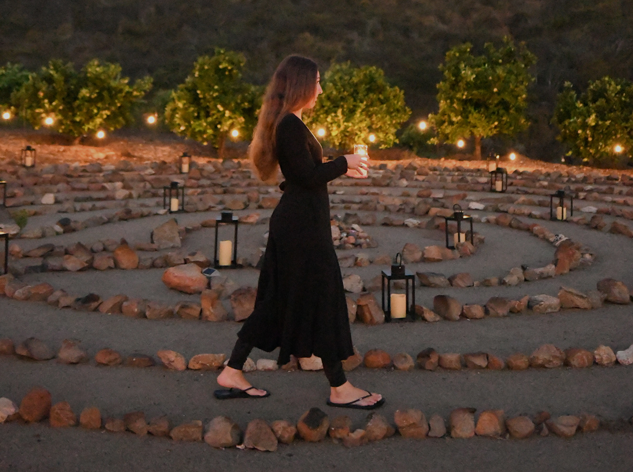 a woman walking in a maze with candles and trees