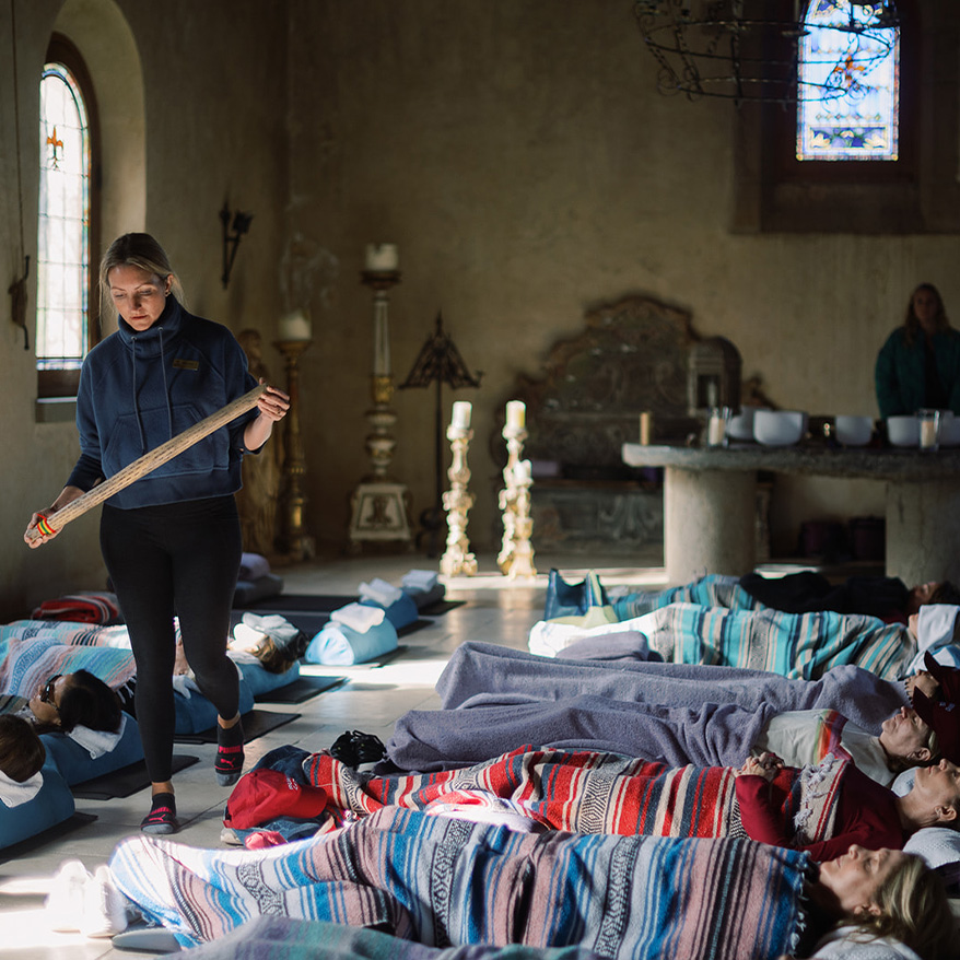 a woman holding a stick in a room with several people lying on the floor