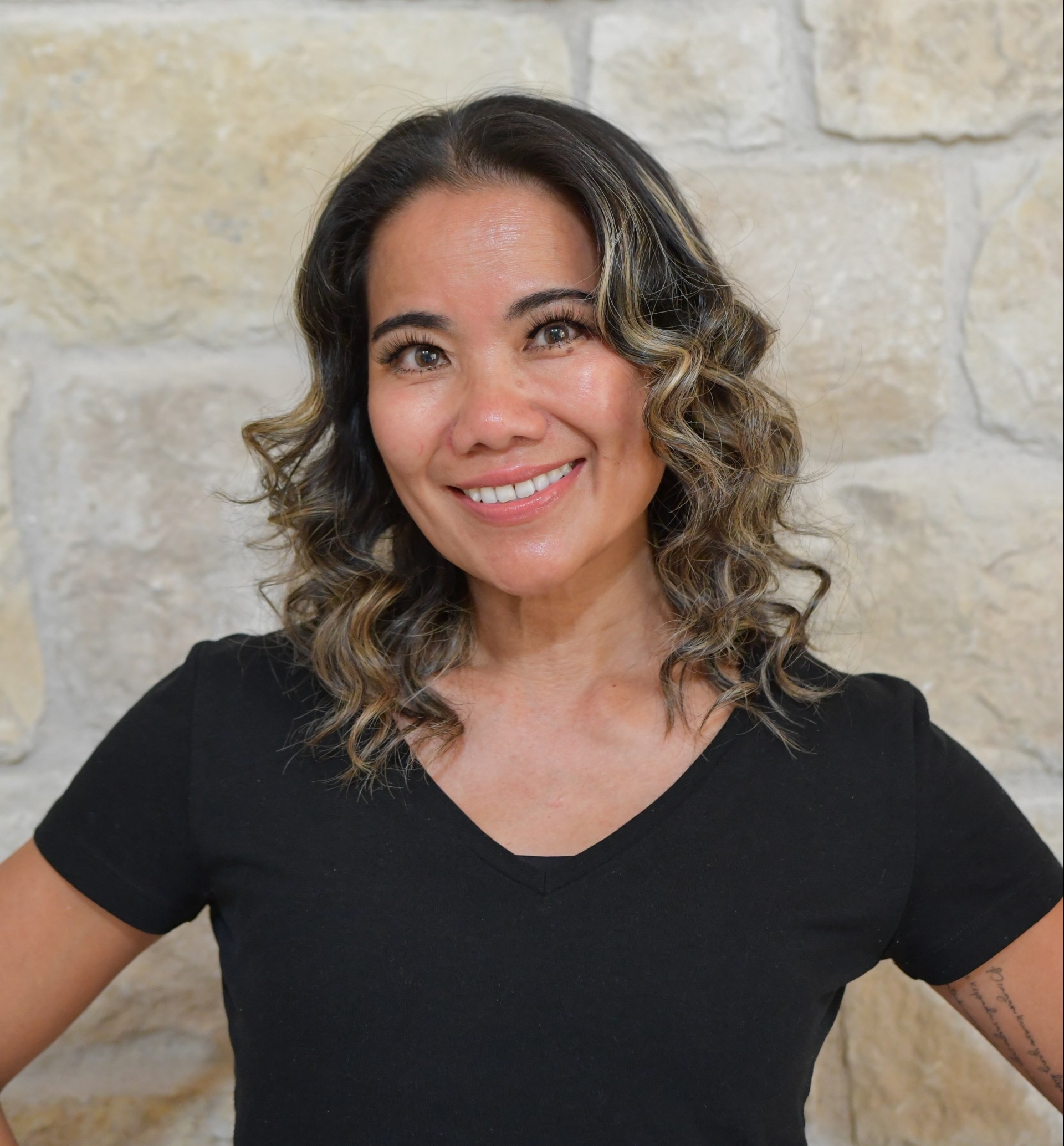 a woman smiling in front of a stone wall