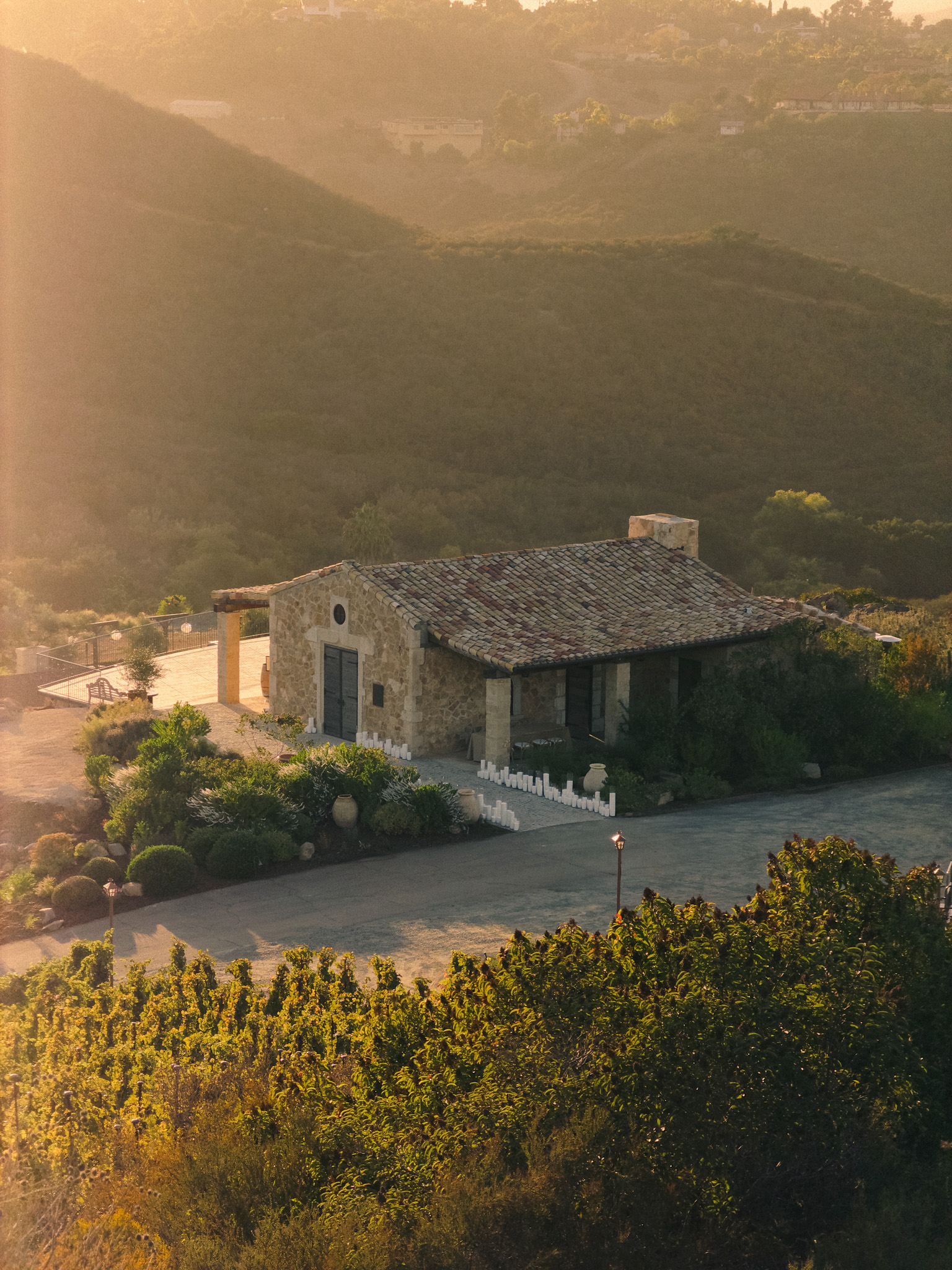 a house with a stone roof and a driveway with trees and mountains in the background