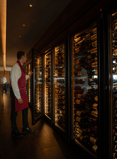 a man in an apron looking at a display of wine bottles
