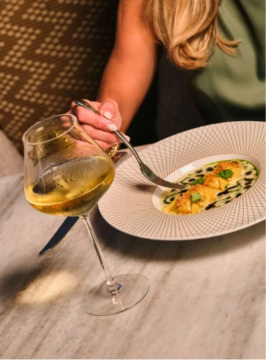 a person eating food on a plate with a glass of wine