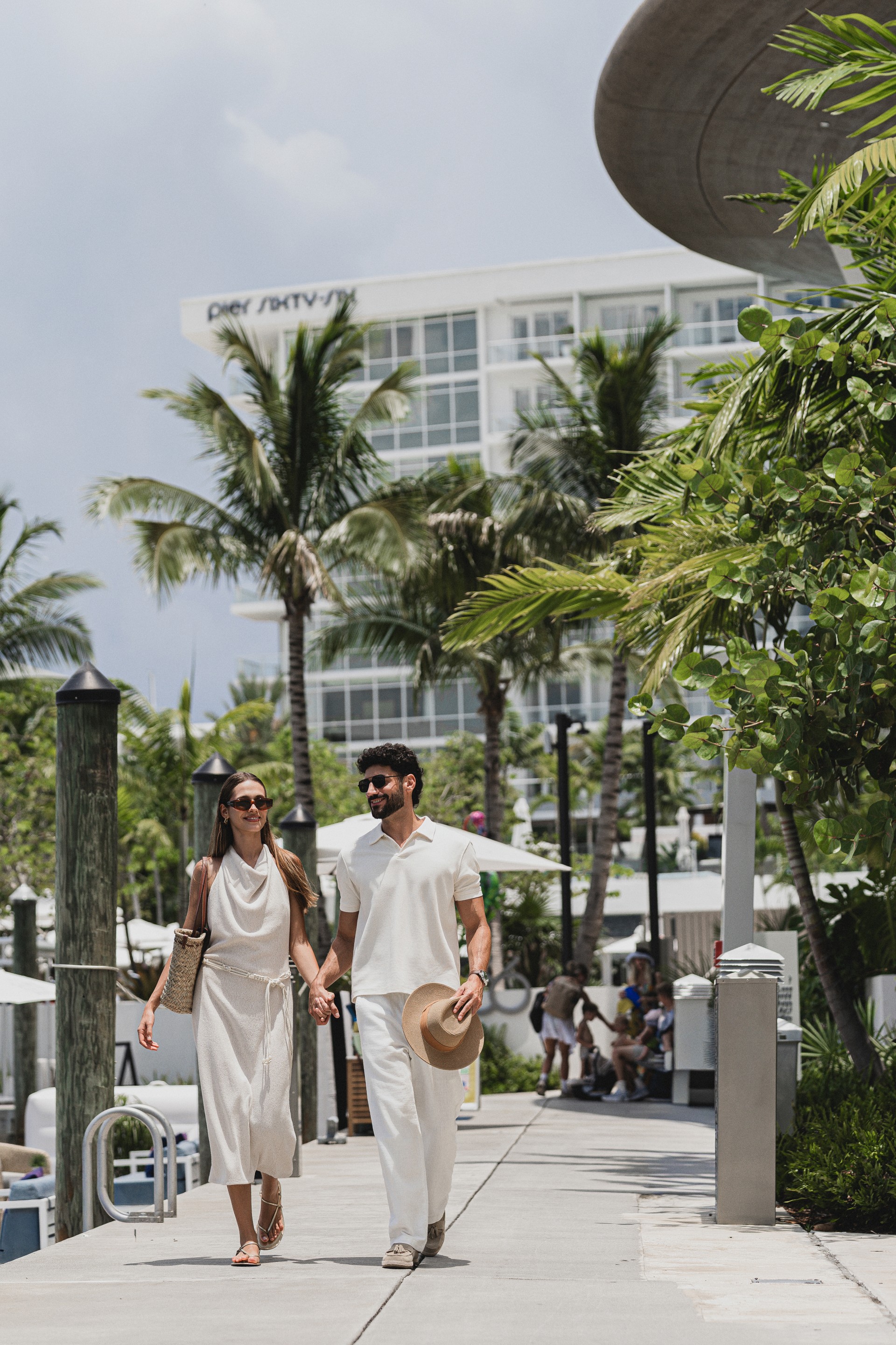 a man and woman holding hands and walking down a sidewalk