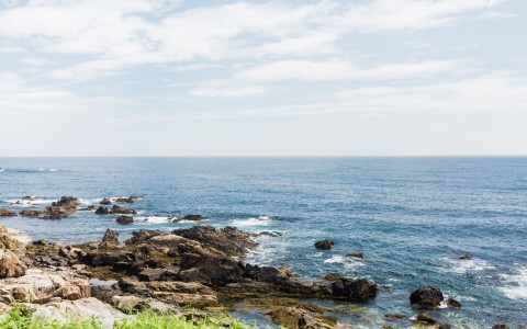 a rocky beach with blue water and clouds
