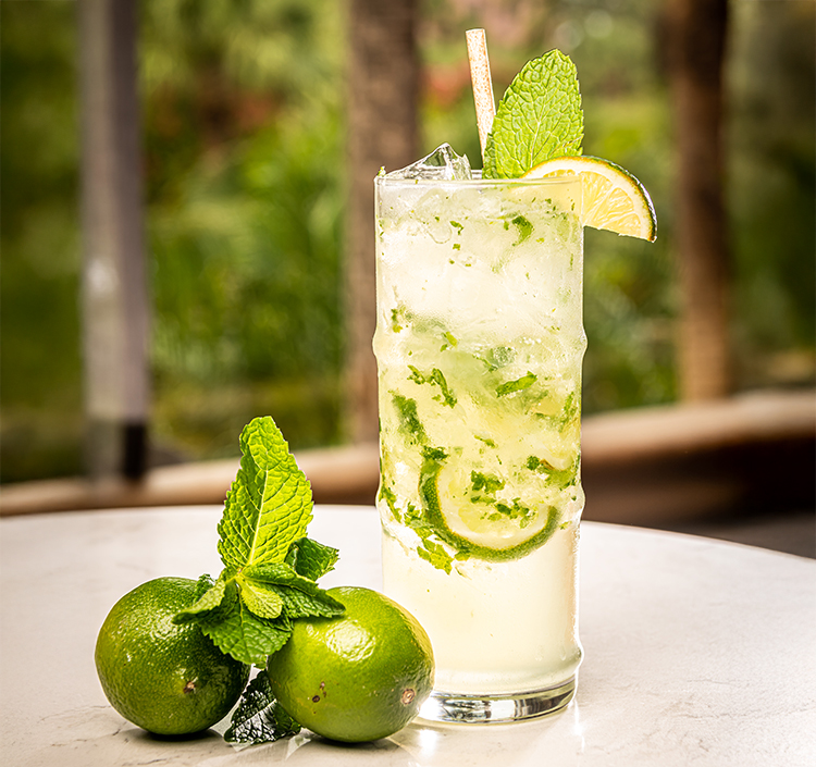 a glass of drink with limes and mint leaves