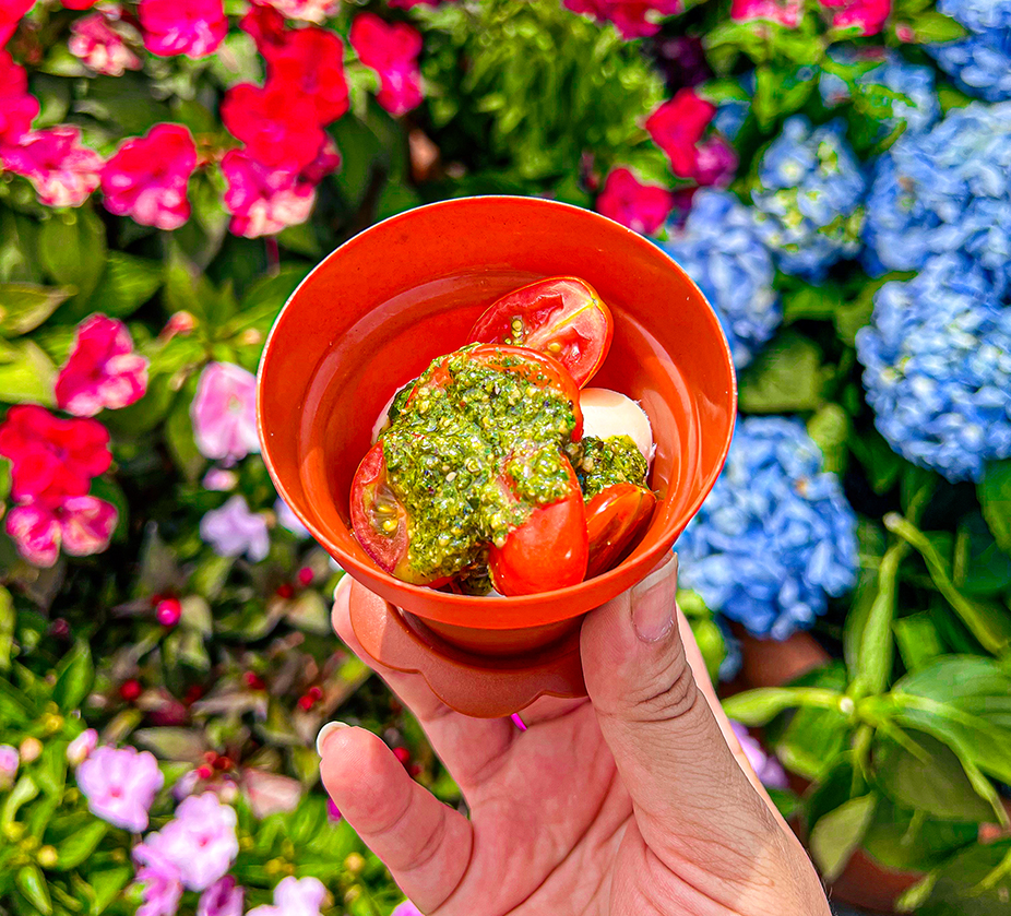 a hand holding a small orange bowl with tomatoes and cheese