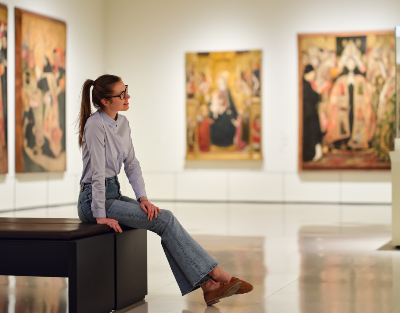 a woman sitting on a bench in front of paintings