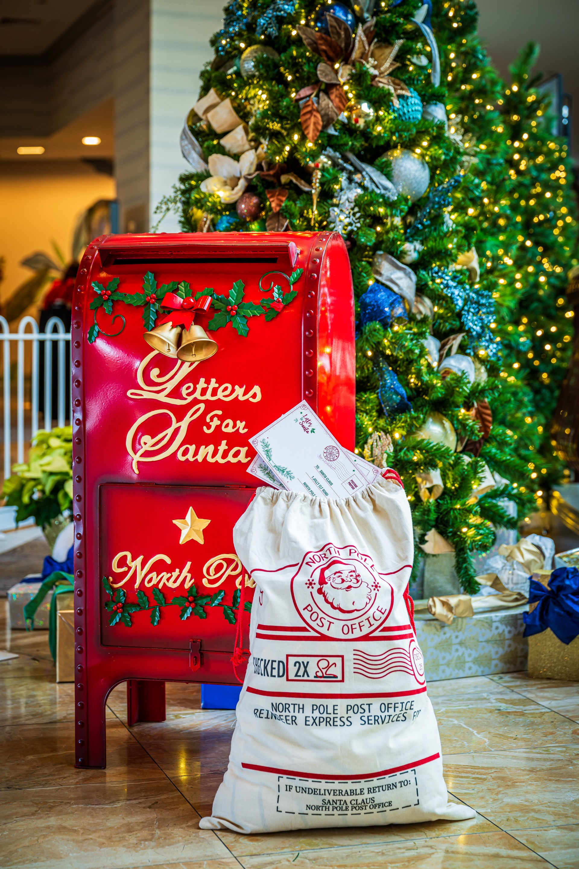 a red mailbox with a bag of letters and a christmas tree