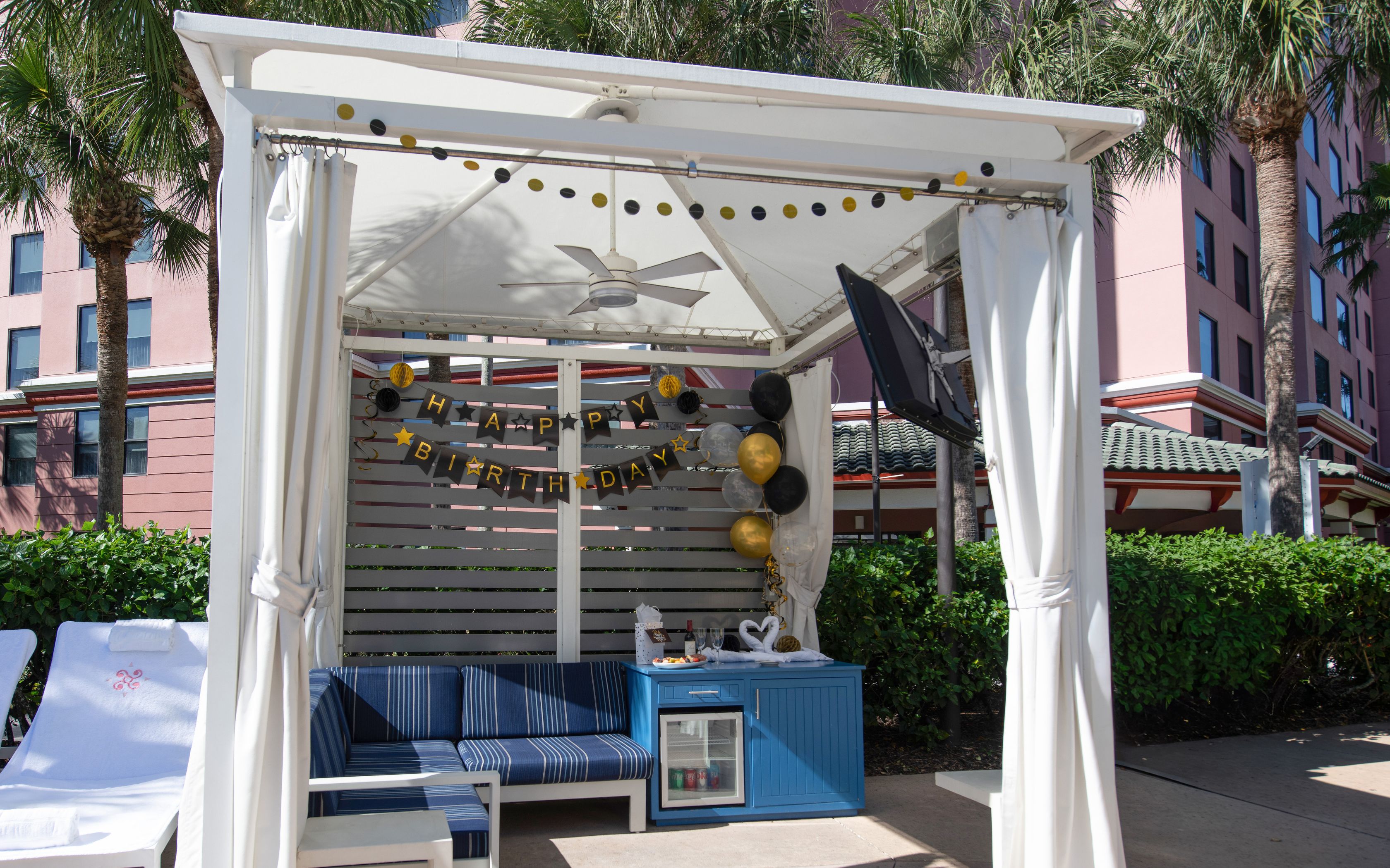 a white tent with blue couches and black and gold balloons