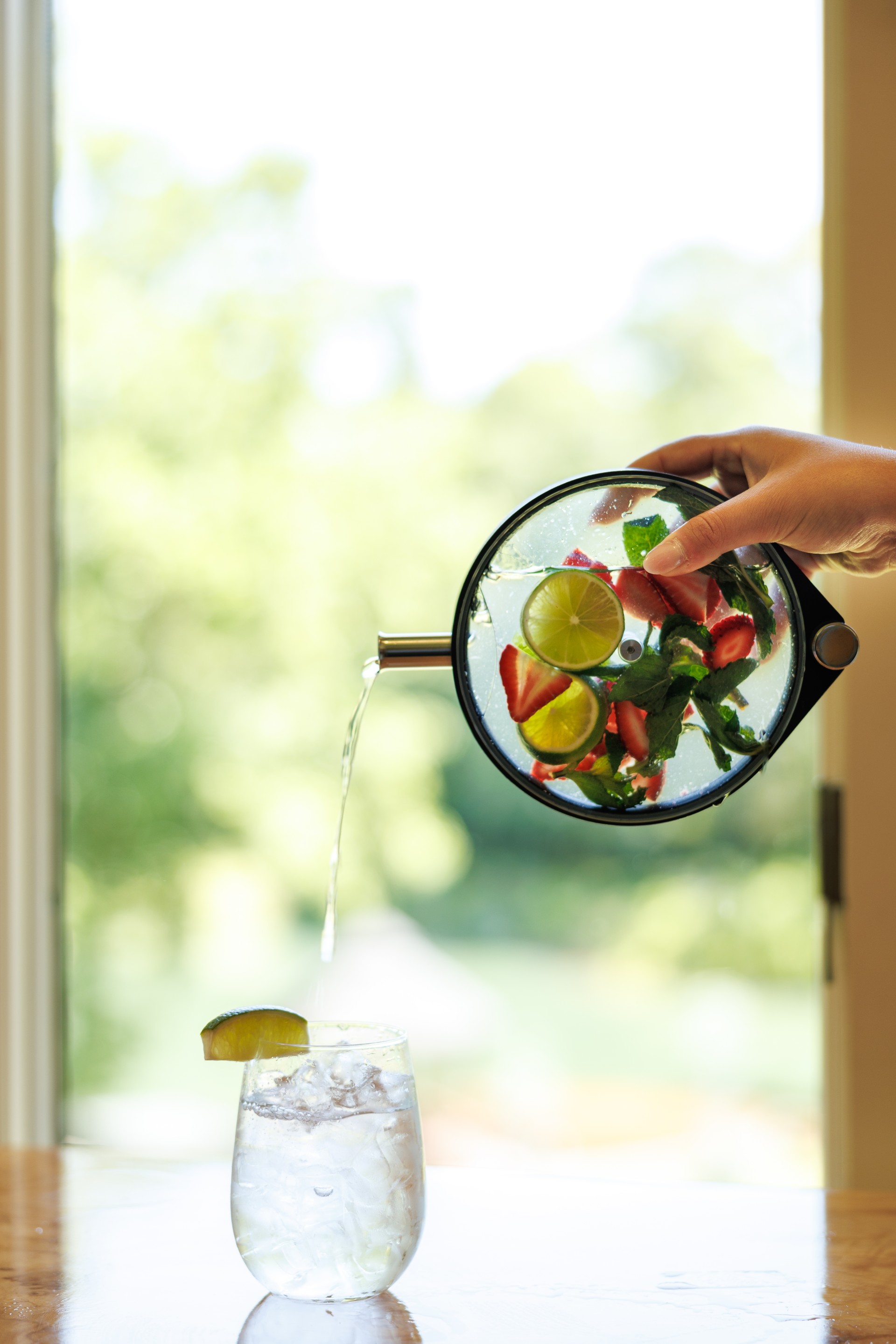 a hand pouring water into a glass with fruit