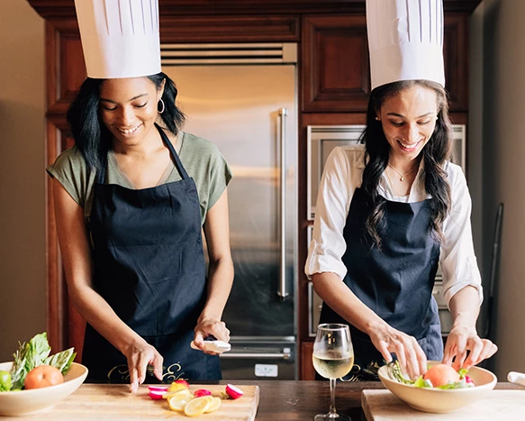 two women wearing chef hats and aprons putting together a salad