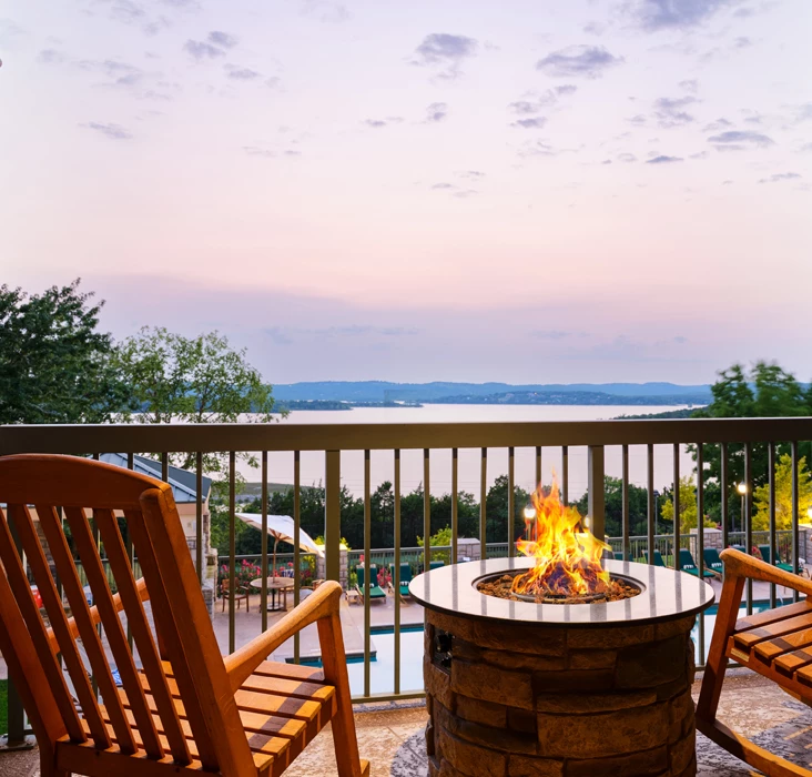 a fire pit with a fire in it by a deck with a body of water and trees
