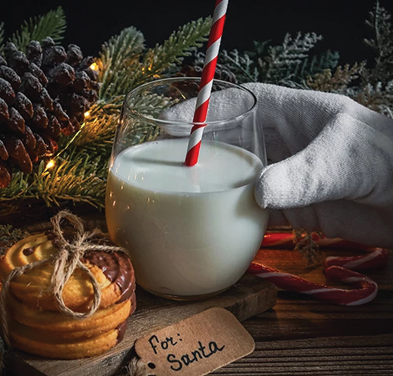 a hand holding a glass of milk with a straw and cookies