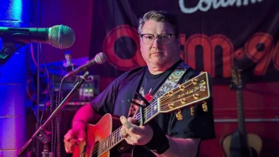 a man playing a guitar and singing into a microphone dave elelberg