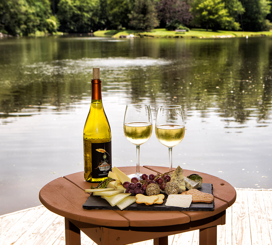 a wine bottle and glasses of wine on a table by water
